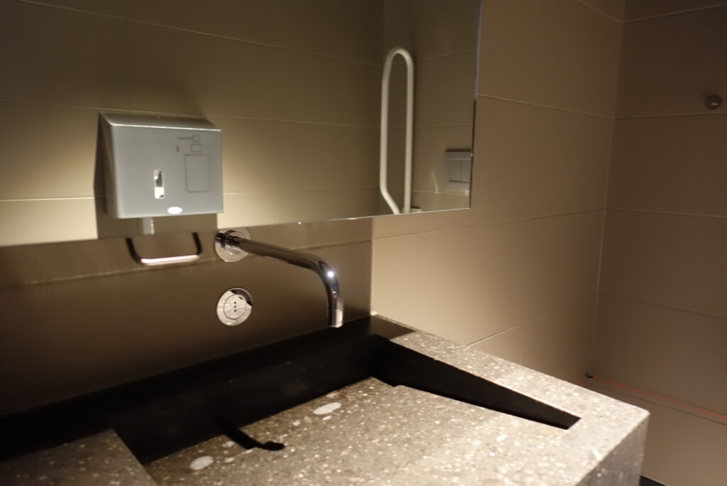 Sinks in all restrooms have touch-less, automatic sensors to start water flow. Soap dispensers with a pump bar are on the front wall to the left of the faucet. Paper towels are on the front wall to the right of the faucet.